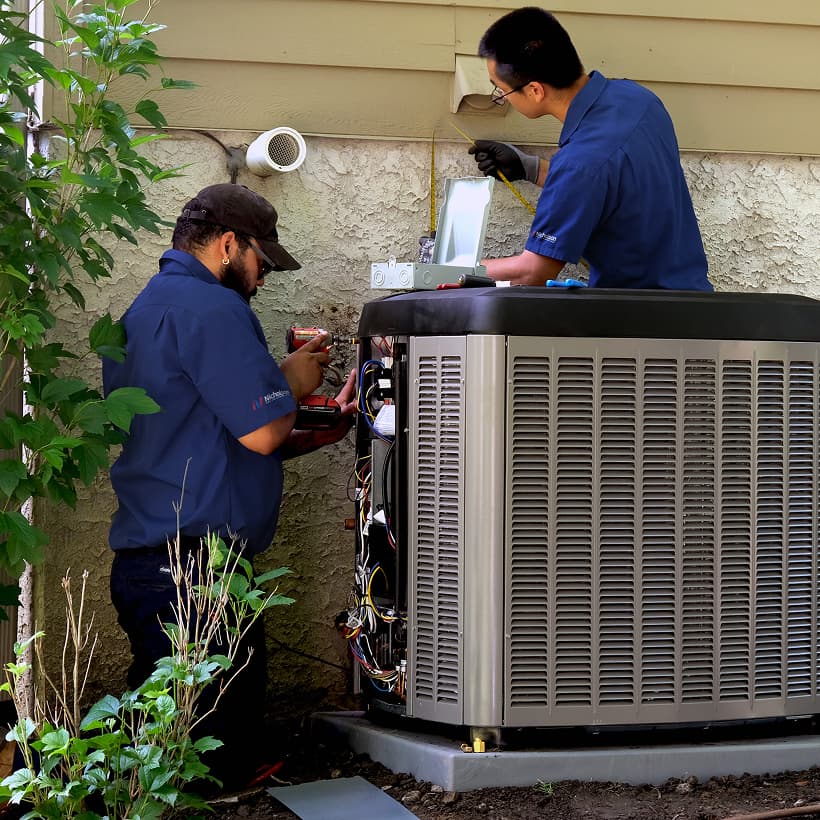 Two Nicholson HVAC technicians installing a brand-new residential outdoor air conditioning condenser unit during a home AC replacement service.