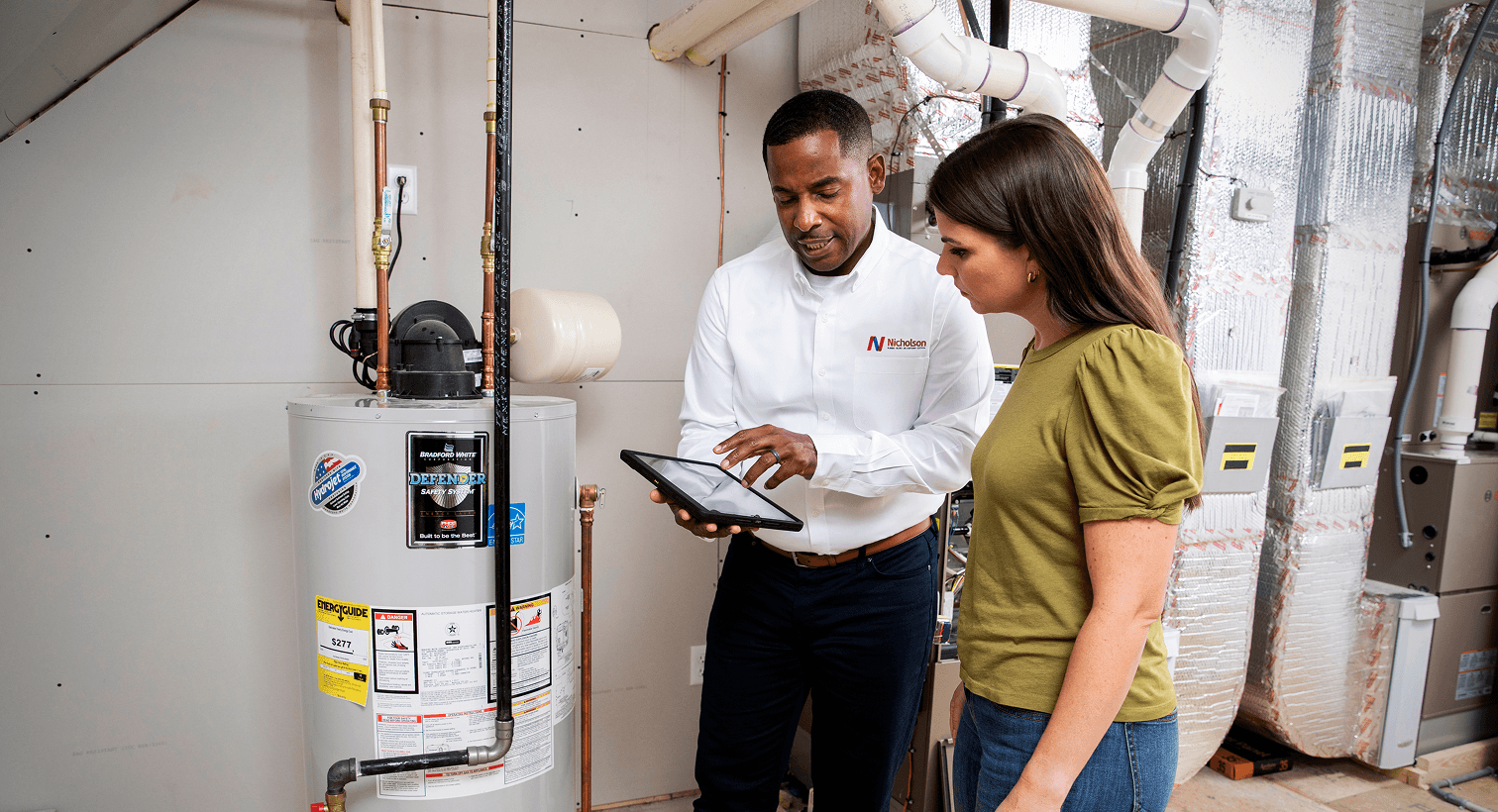A Nicholson plumber using a tablet to discuss residential water heater services, repairs, and replacement options with a homeowner.